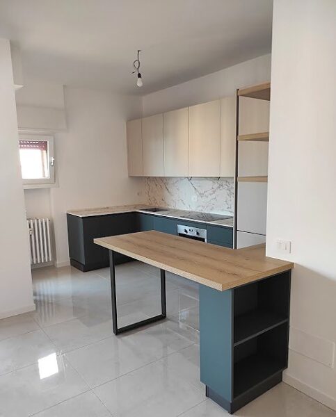 Cucina moderna su misura con basi verde petrolio, pensili chiari, top effetto marmo e penisola in legno